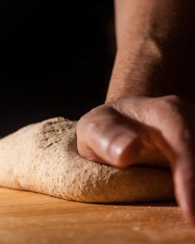 Mâini care frământă o pâine pe un blat de lemn
